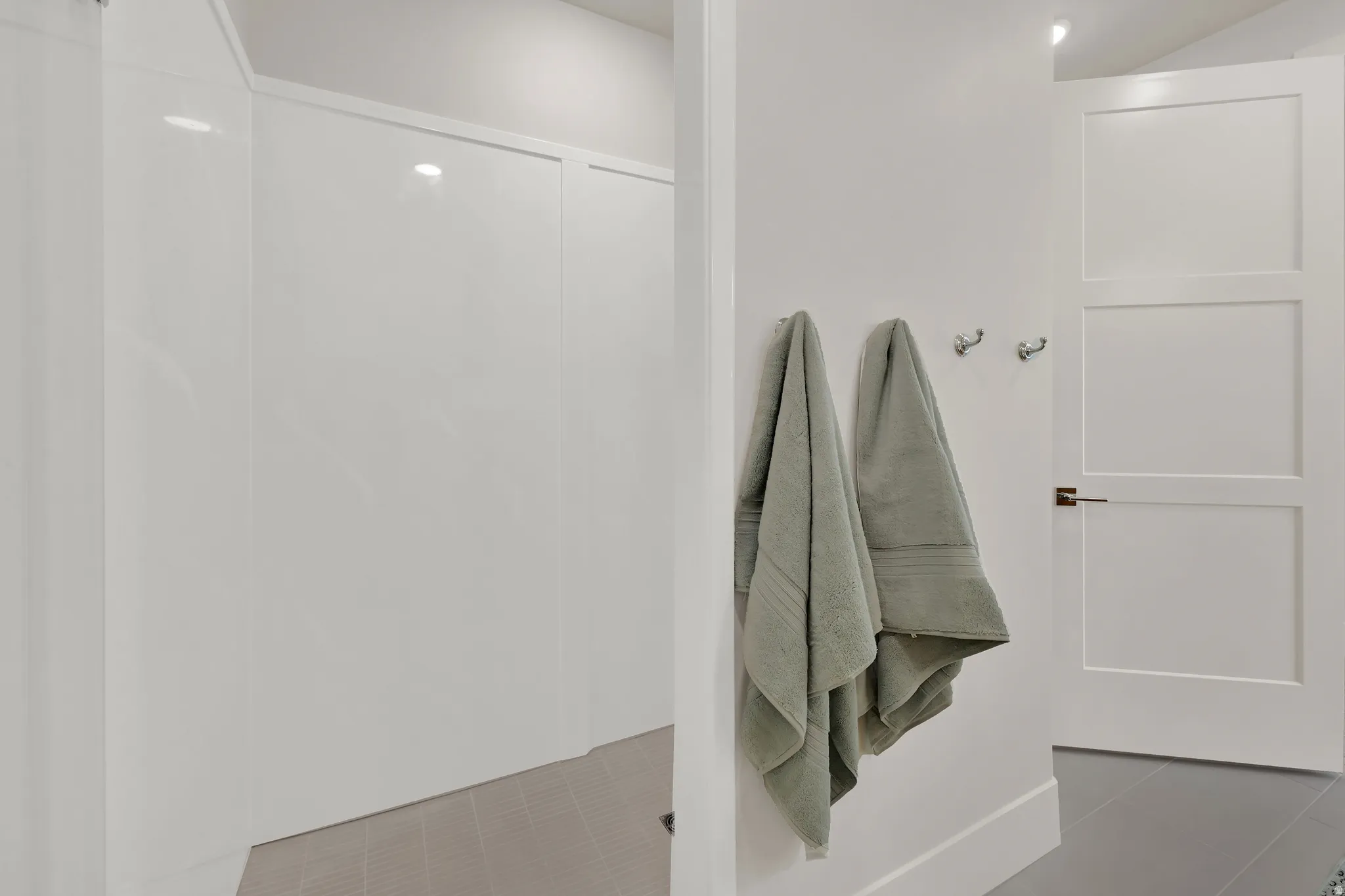 White panel shower enclosure with a tiled floor, adjacent to a three-panel interior door with brushed nickel hardware
