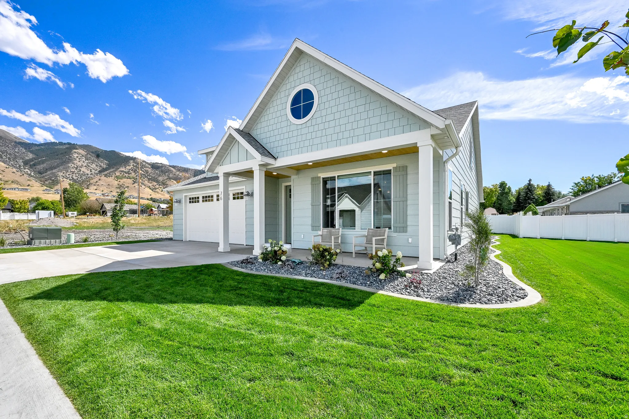 Light blue siding exterior with white trim, a covered front porch, a two-car garage, and a lush green lawn