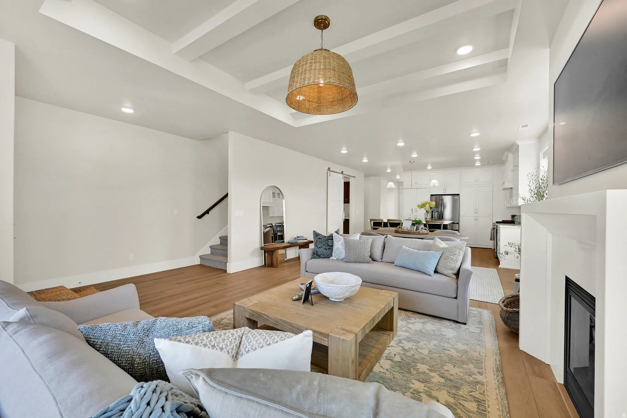 Coffered ceiling with a woven pendant light, wood-finish flooring, and a fireplace with a white mantel