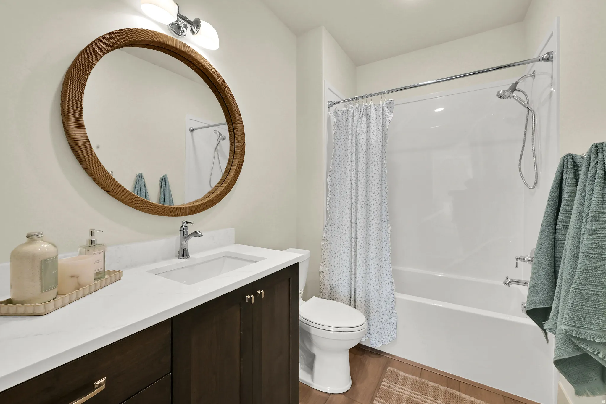 Bathroom featuring a vanity with a white countertop and integrated sink, dark wood-finish cabinetry, a round mirror, and a shower-tub combination with a wall-mounted showerhead