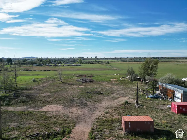 Expansive green fields with distant hills, featuring a large metal-sided structure and a red storage container