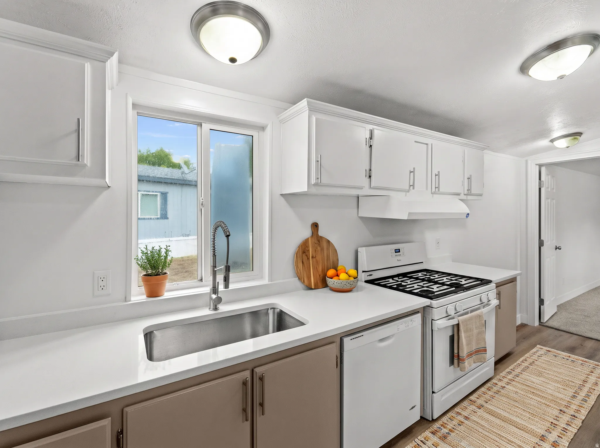 Kitchen featuring white upper cabinetry, two-tone lower cabinetry, light countertops, stainless steel sink, and white appliances