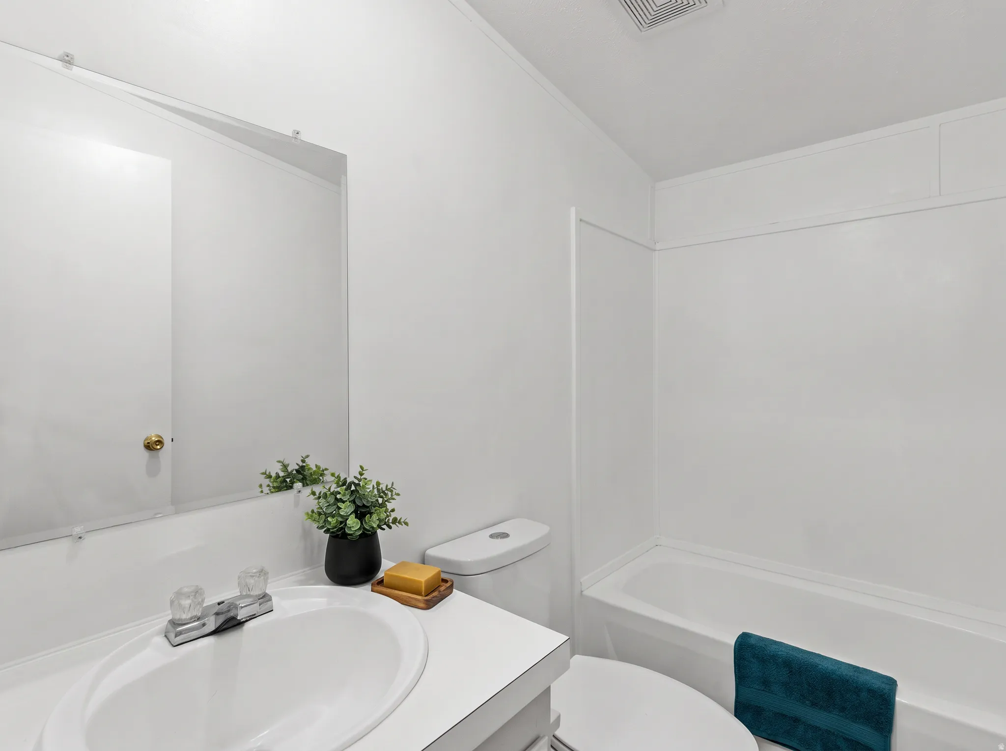 White vanity with an integrated sink and chrome faucet, a wall-mounted mirror, and a white bathtub with a shower surround