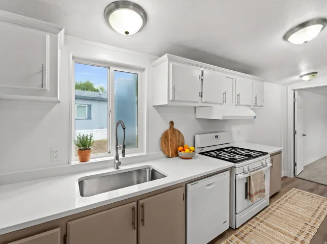 Kitchen featuring white upper cabinetry, two-tone lower cabinetry, light countertops, stainless steel sink, and white appliances