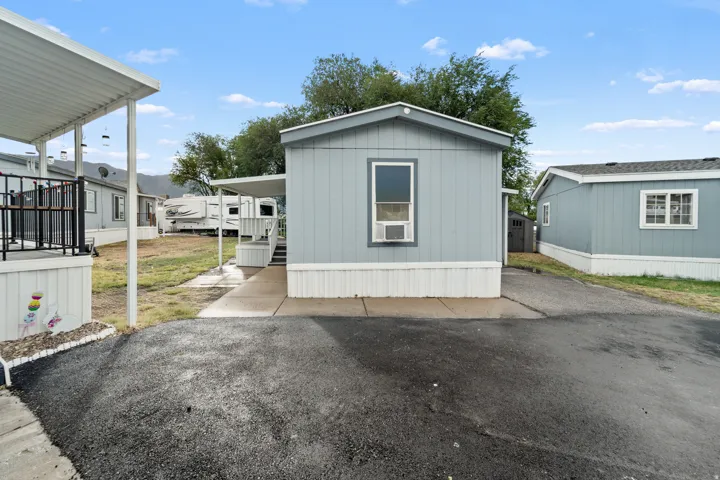 Light blue exterior with white trim, single window with an attached air conditioning unit, covered porch area, and a paved walkway