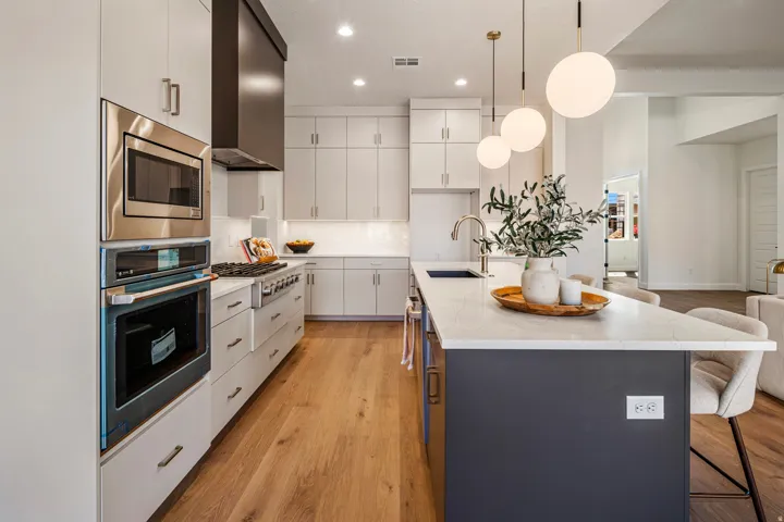 Gourmet kitchen featuring stainless steel appliances, white cabinetry, a spacious island with seating, pendant lighting, and wood-finish flooring