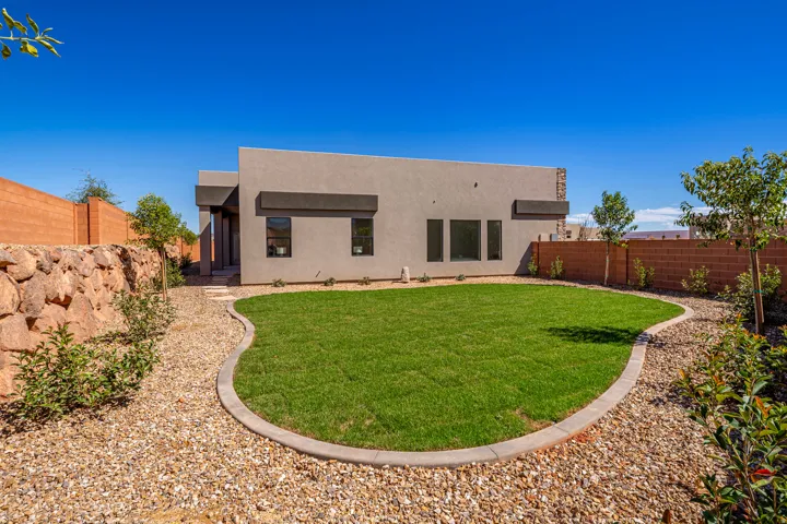 Contemporary stucco exterior featuring a curved lawn area, gravel landscaping, and a low stone wall