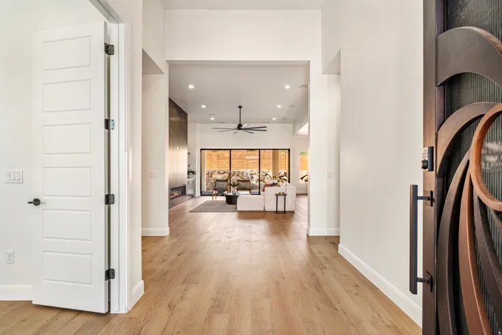 Wide plank wood-finish flooring extending into living areas, recessed lighting, and a decorative security screen door