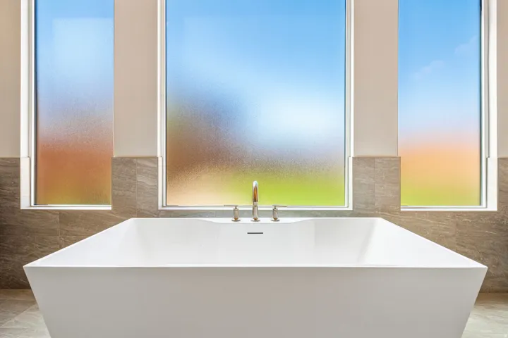 Freestanding soaking tub with a floor-mounted faucet, complemented by large format wall tile, and multiple privacy-frosted windows
