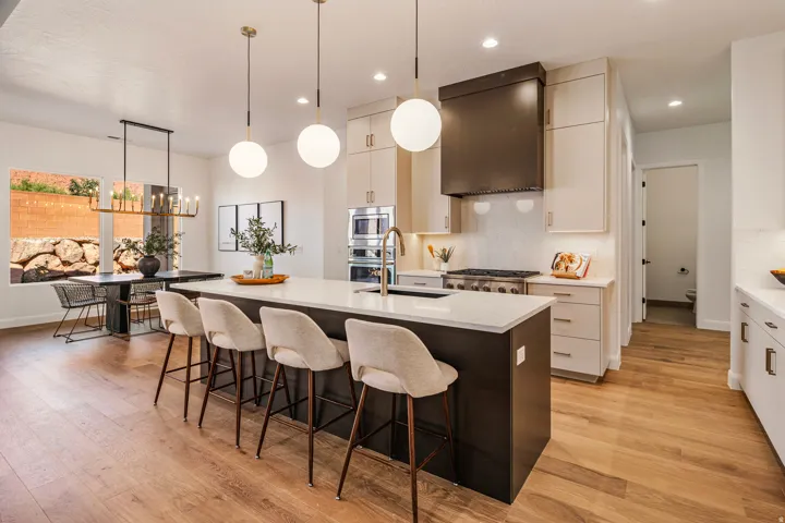 Open-concept kitchen featuring an oversized island with seating, a gas range with a modern range hood, integrated double ovens, light-finish cabinetry, and wood-finish flooring