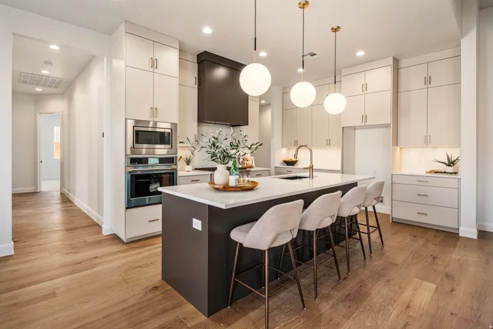 Modern kitchen featuring light wood-finish flooring, a large island with countertop seating, integrated stainless steel appliances, and sleek overhead and under-cabinet lighting