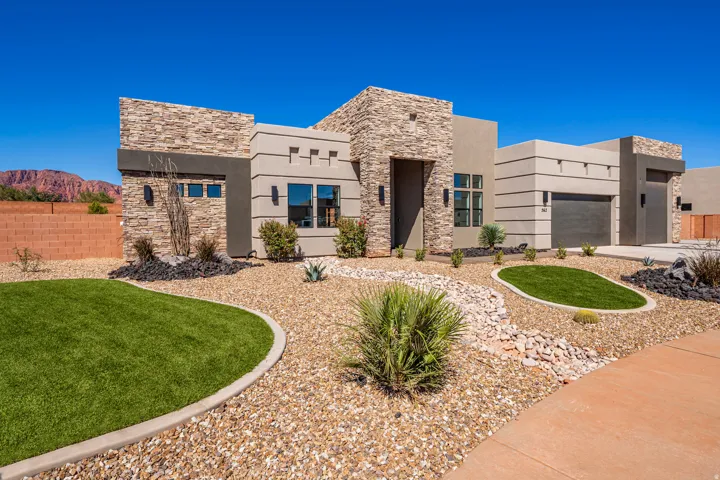 Stone and stucco exterior, two-car garage, desert landscaping, decorative exterior lighting, and a red rock mountain backdrop