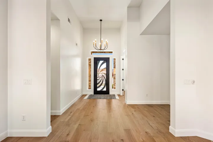 Entryway featuring wood-finish flooring, a decorative front door with side panel windows, a chandelier, and vaulted ceilings