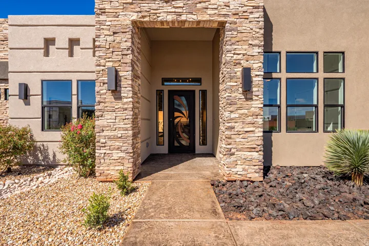 Stacked stone entry, contemporary front door with sidelights, modern exterior lighting, stucco facade, and varied window configurations