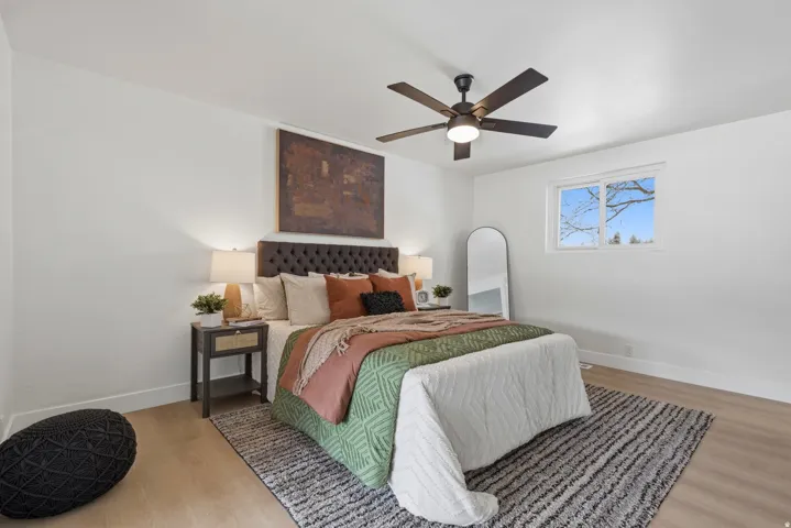 White walls, wood-finish flooring, and a ceiling fan with integrated lighting