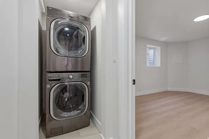 Stacked washer and dryer unit, wood-finish flooring, white walls, recessed ceiling light, and a window