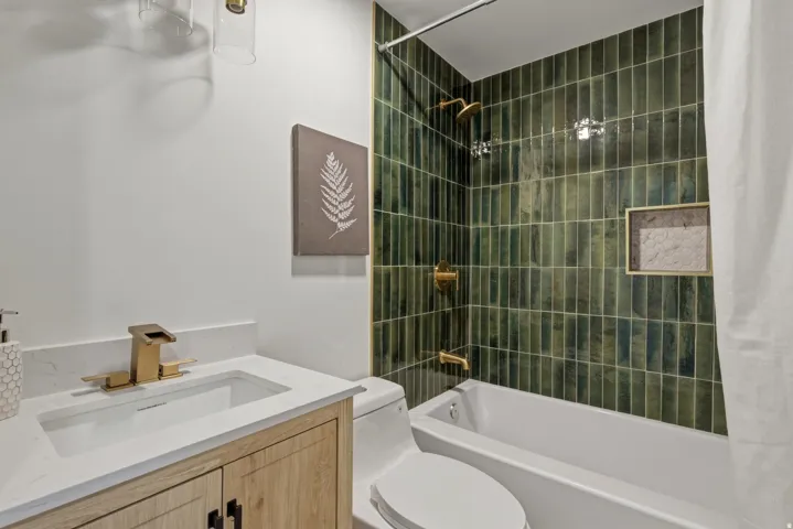 Bathtub with green subway tile surround, built-in shower niche, and brass fixtures