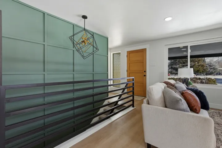Accent wall with geometric paneling, wood-finish flooring, metal railing, three-panel wooden door, and recessed lighting