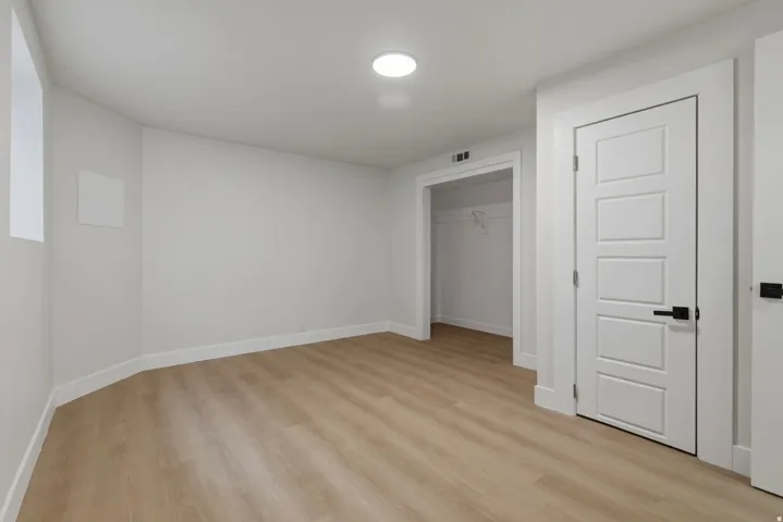 Recessed ceiling lighting, wood-finish flooring, white panel door with black hardware, and an open closet