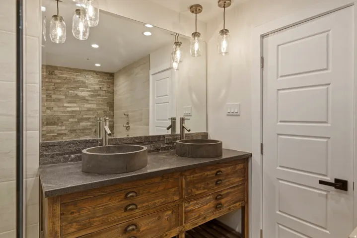Dual vessel sinks with wall-mounted faucets, rustic wood vanity with integrated drawer pulls, and a full-width mirror