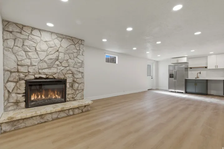 Stone-clad fireplace with hearth, wood-finish flooring, recessed lighting, and a stainless steel refrigerator