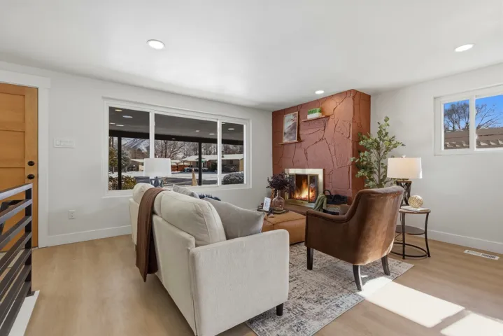 Warm living area featuring a stone-clad fireplace, wood-finish flooring, recessed lighting, and a prominent window