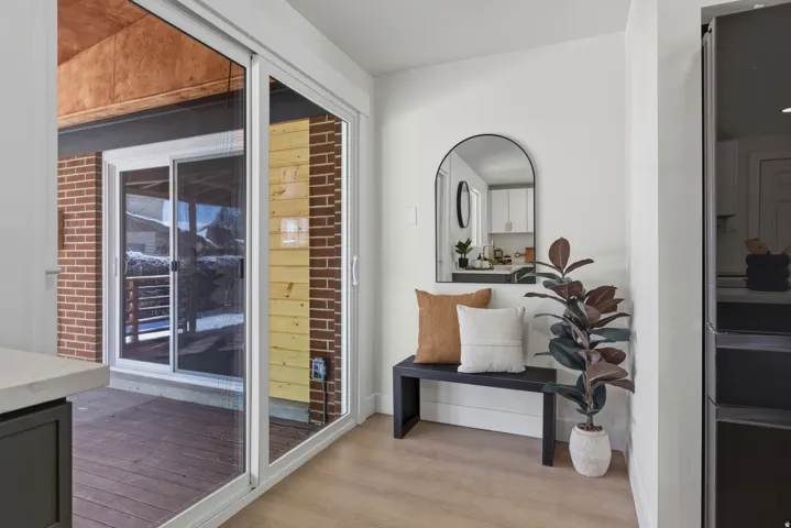 Sliding glass doors opening to an exterior deck, brick and wood paneling exterior, light wood-finish flooring, and a built-in black cabinet