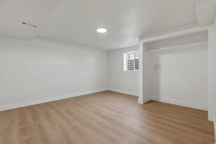Spacious room featuring light wood-finish flooring, recessed lighting, and an open closet with integrated shelving