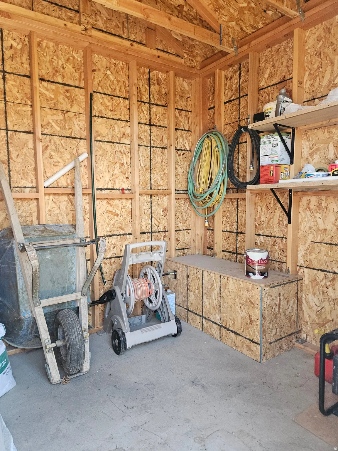 Exposed wood framing with oriented strand board sheathing, concrete flooring, and built-in shelving and storage bench