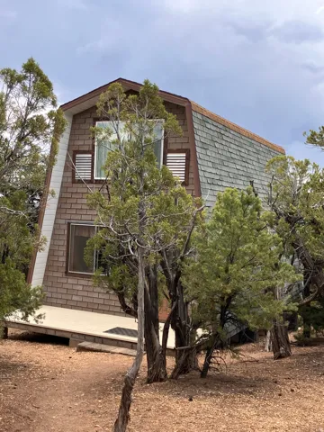A-frame structure with shingle siding, an elevated deck, and mature trees
