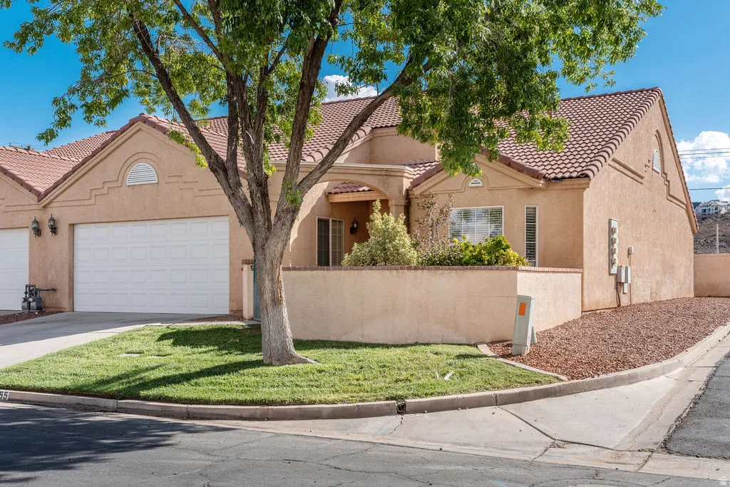 Stucco exterior with a tiled roof, integrated garage, and a landscaped front yard featuring a tree and groundcover