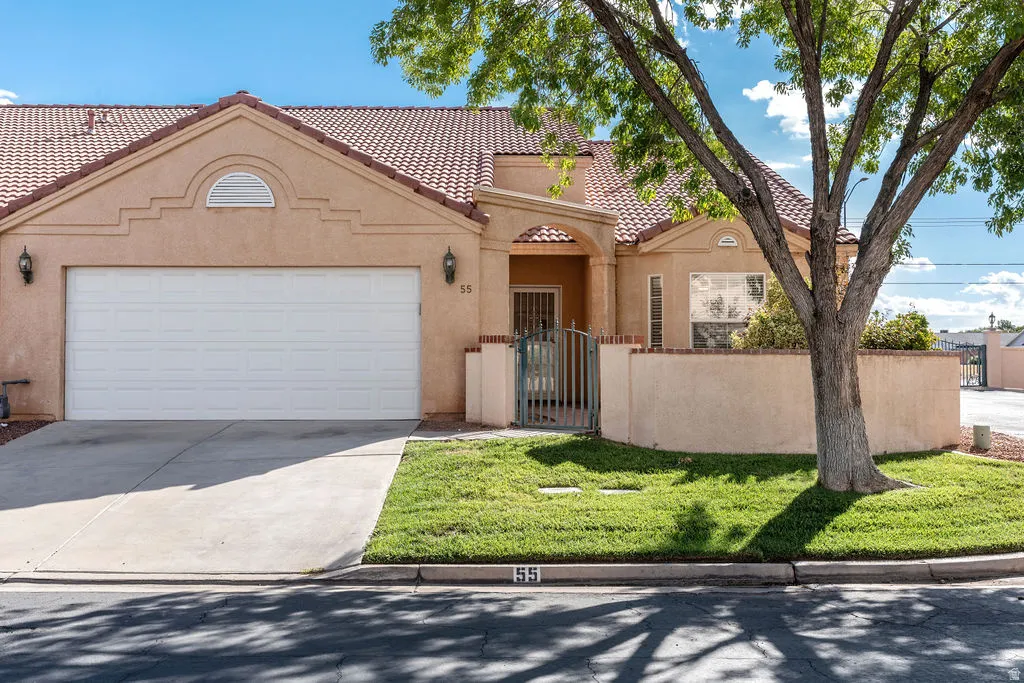 Stucco exterior with a tiled roof, integrated two-car garage, gated entry, and a manicured lawn