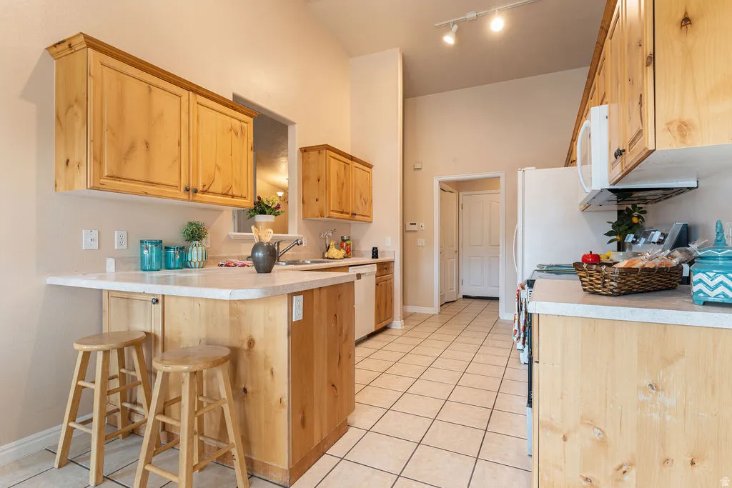 Kitchen featuring wood cabinetry, white tile flooring, track lighting, a partial peninsula, and white appliances