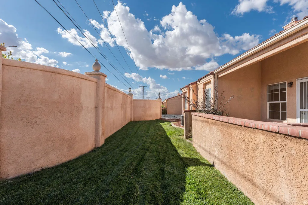 Private side yard featuring a manicured lawn, stucco walls with decorative finials, and a brick-capped partition wall
