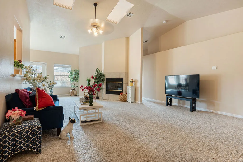 Vaulted ceilings with skylights, ceiling fan light fixture, integrated fireplace with tile surround, and multiple windows providing natural illumination