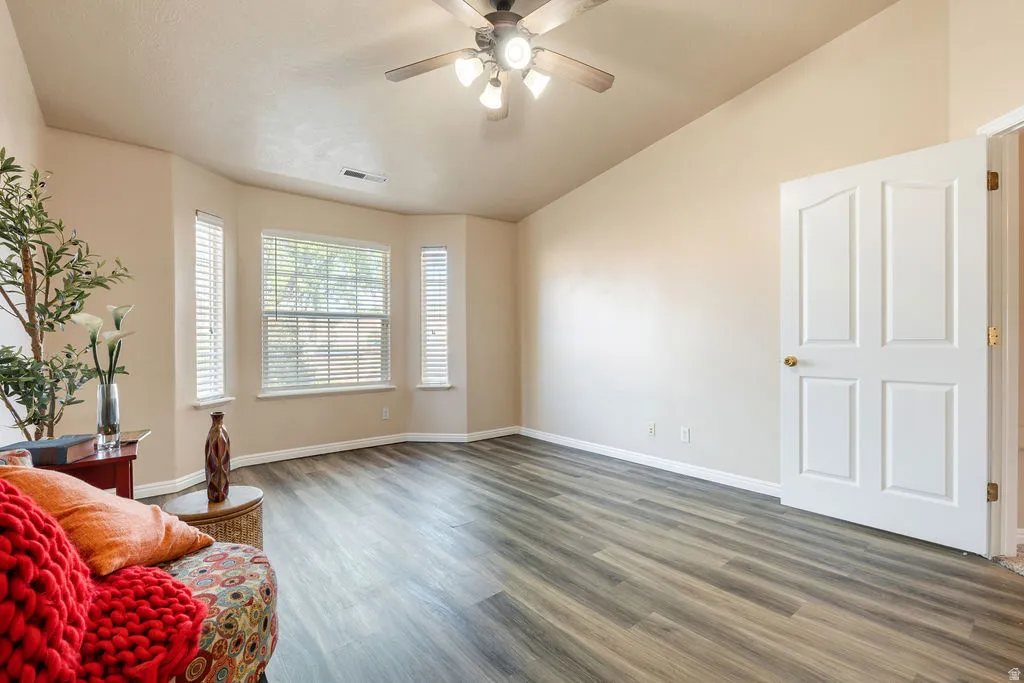 Vaulted ceiling with a ceiling fan, bay window with blinds, wood-finish flooring, and a paneled door