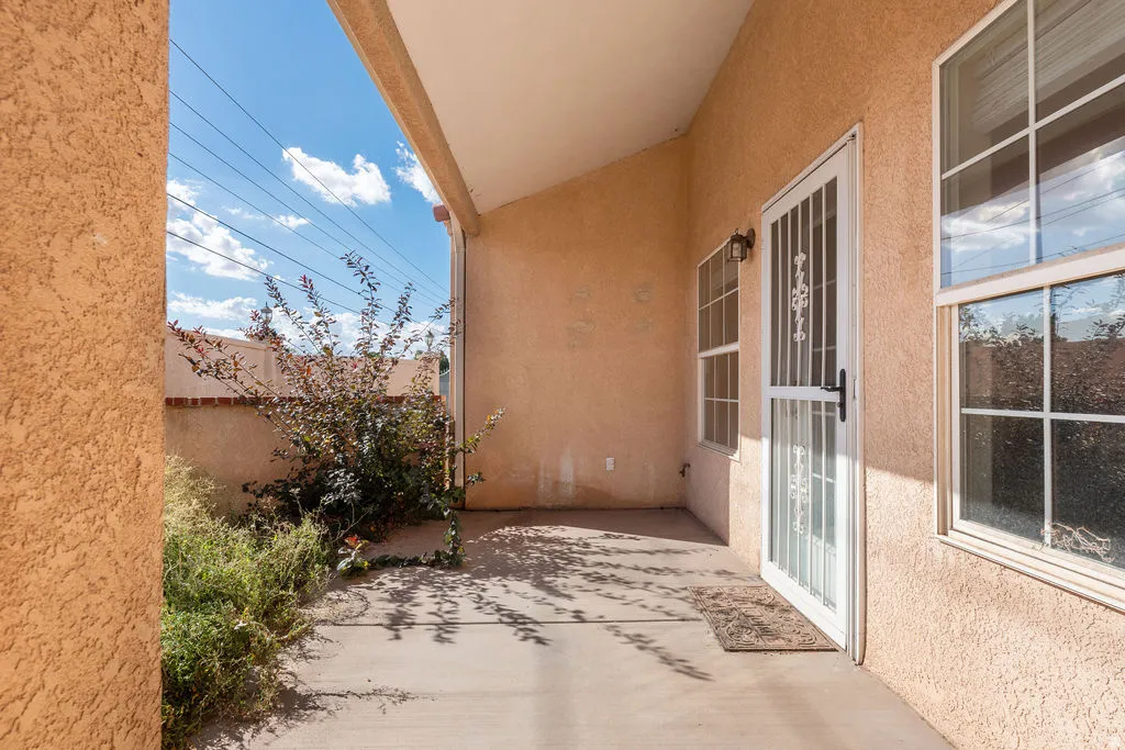 Covered outdoor patio with textured exterior walls, white-framed windows, and a security screen door