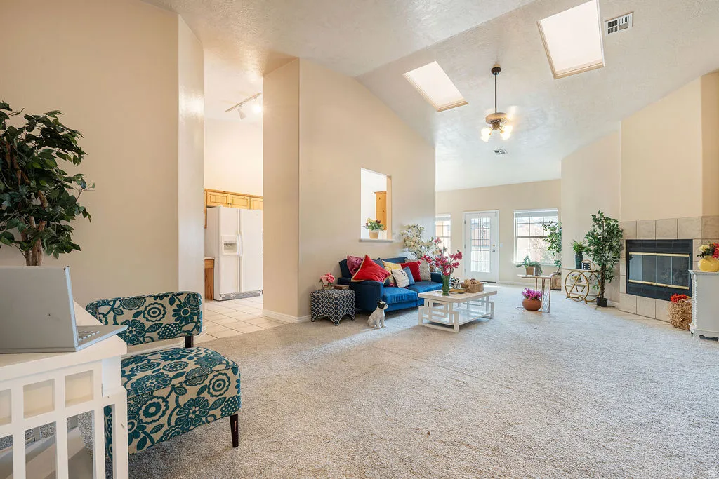 Vaulted ceiling with skylights and ceiling fan, carpeted flooring, tiled fireplace with hearth, and multiple windows