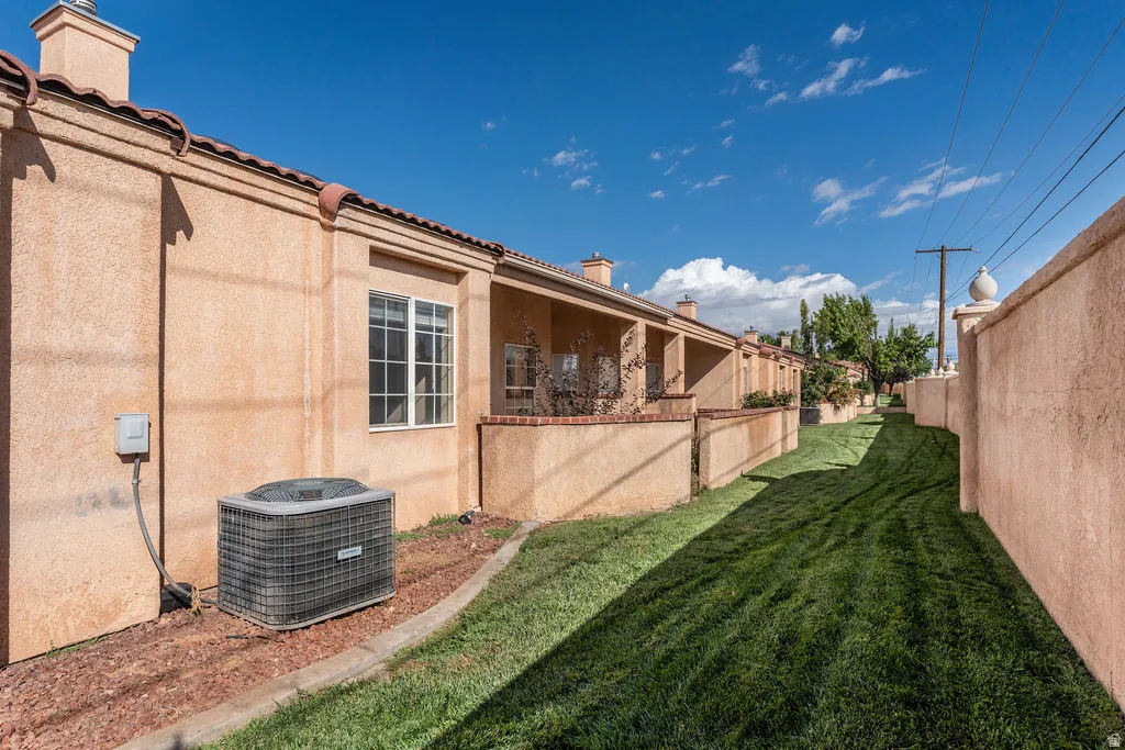 Stucco exterior with a tiled roof, white-framed windows, and a manicured grassy corridor