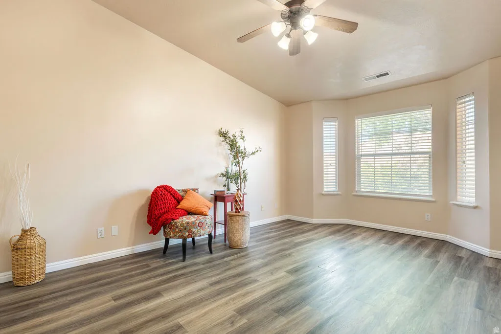 Vaulted ceiling, wood-finish flooring, bay window with blinds, ceiling fan with integrated lighting, and neutral wall tones