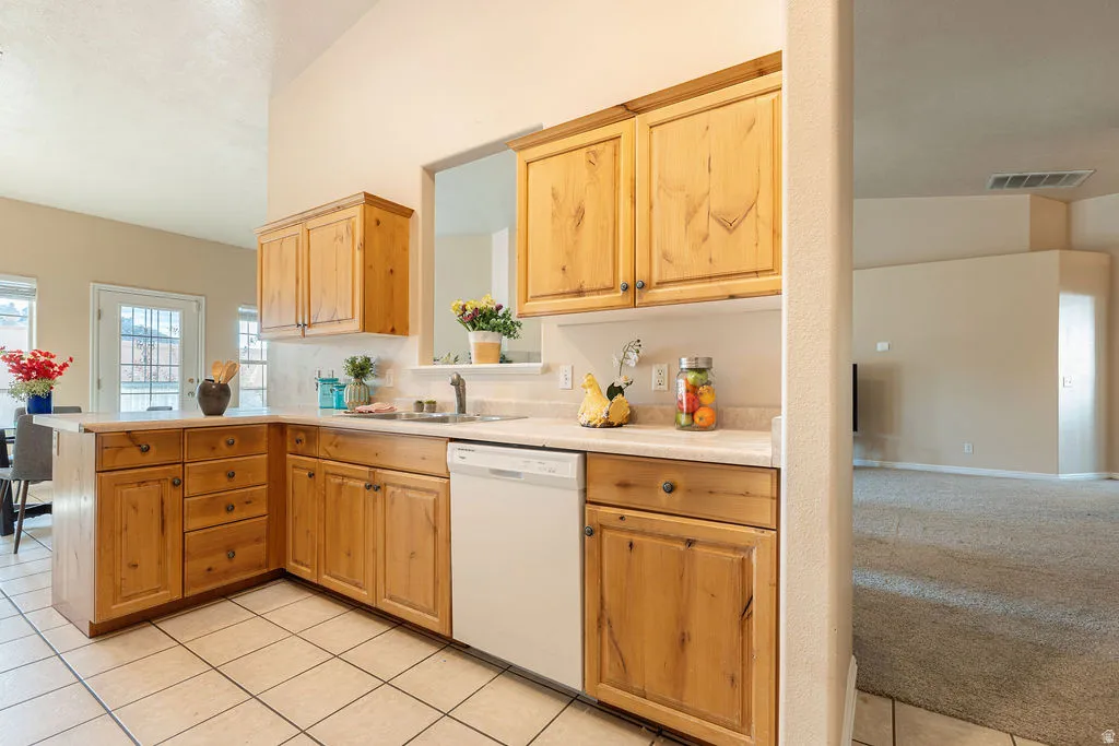 Kitchen featuring wood cabinetry, white countertops, tile flooring, and a white dishwasher
