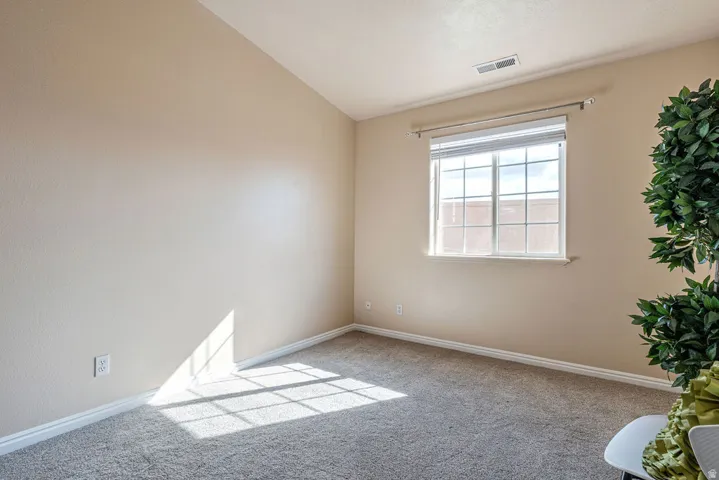Vaulted ceiling, neutral wall finish, window with grid panes, textured carpet, and a wall outlet