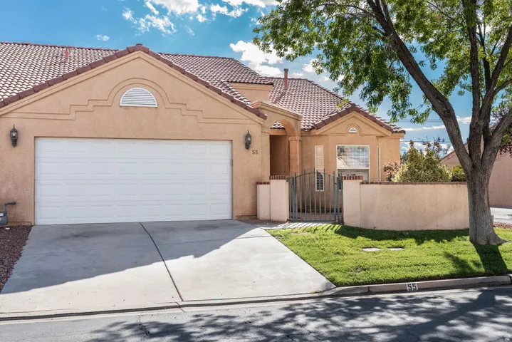 Stucco exterior with a tile roof, an integrated garage, a wrought iron entry gate, and a landscaped front yard with mature trees