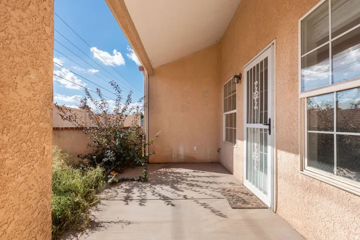 Covered outdoor patio with textured exterior walls, white-framed windows, and a security screen door