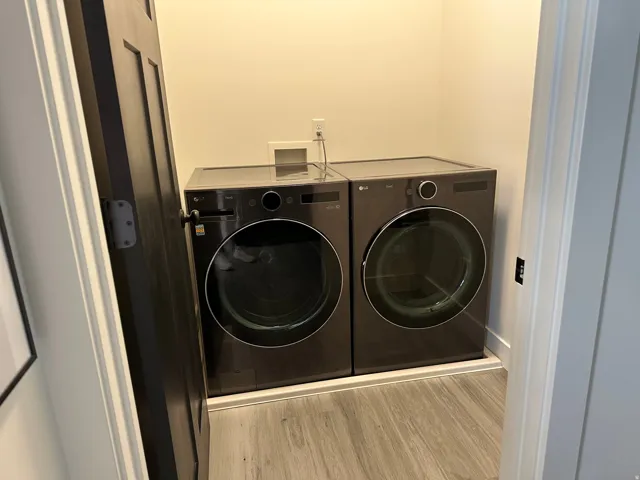 Dedicated laundry area featuring a front-loading washer and dryer set, wood-finish flooring, and a dark wood-panel door