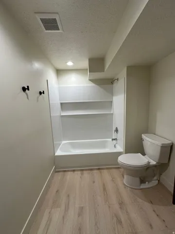 Wood-finish flooring, recessed lighting, and a white bathtub with integrated shelving