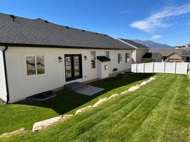 Expansive backyard with a manicured lawn, white privacy fencing, and a concrete patio