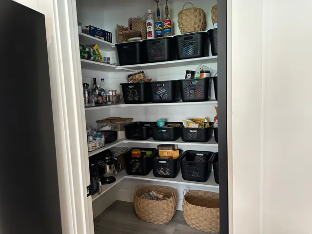 Walk-in pantry with multiple tiers of shelving, vertical paneling, and wood-finish flooring