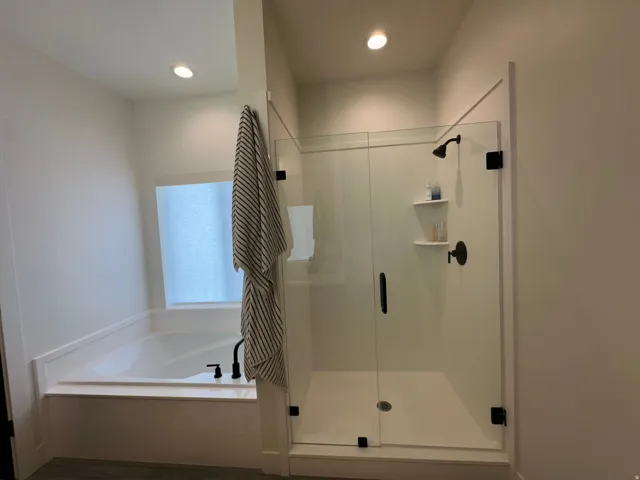 Built-in soaking tub with matte black fixtures, glass-enclosed shower with matte black fixtures, recessed lighting, and a frosted window