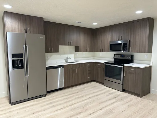 Modern kitchen featuring wood-grain cabinetry, light countertops, stainless steel appliances, and wood-finish flooring